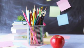 A stack of textbooks, multi-colored pencils, a red apple, on the background of a school board and note paper, educational supplies, education
