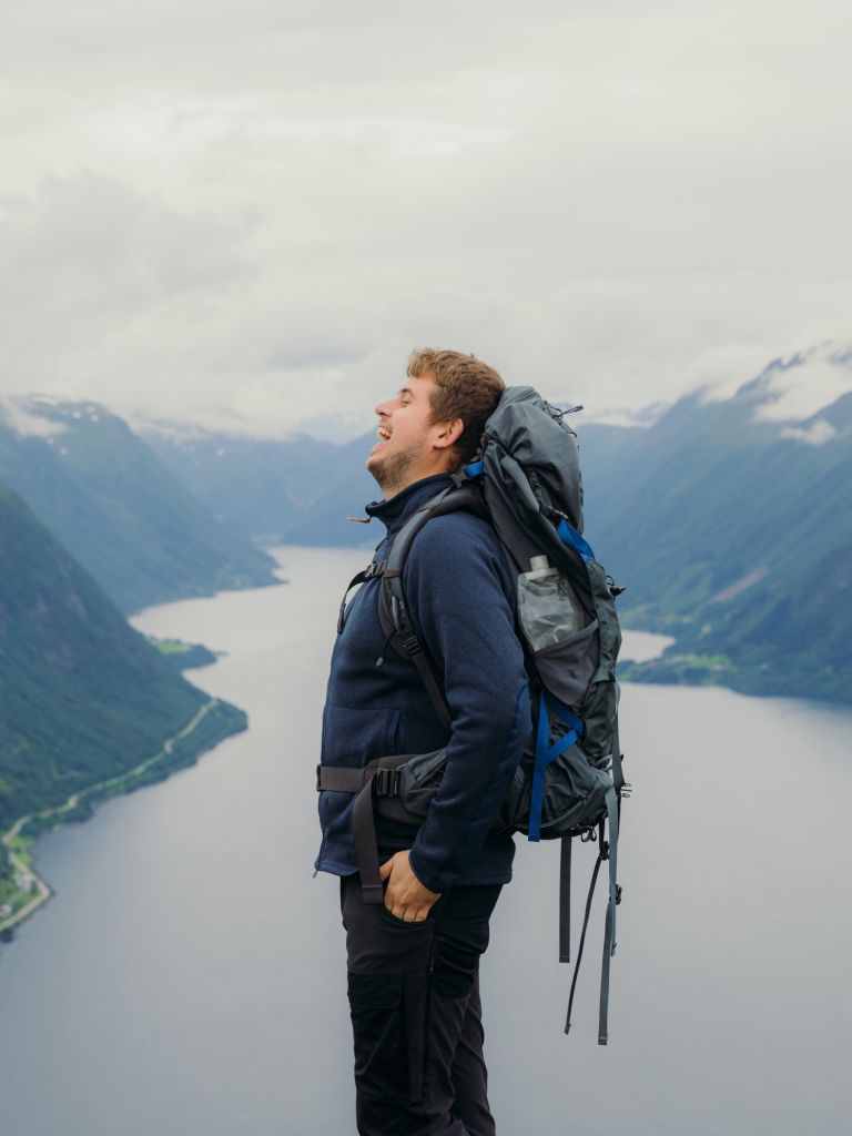 Happy Man with backpack hiking in summer mountains of Norway