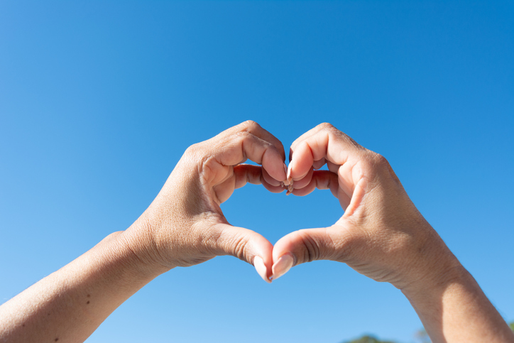 Womans hands showing heart sign on blue sky background