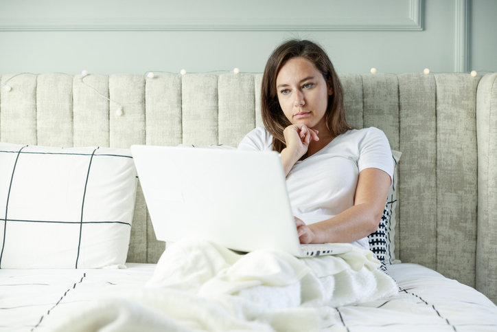 Young woman working on a laptop sitting on the bed