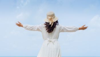 Happy Young woman in a white dress and hat standing on the beach and enjoying freedom