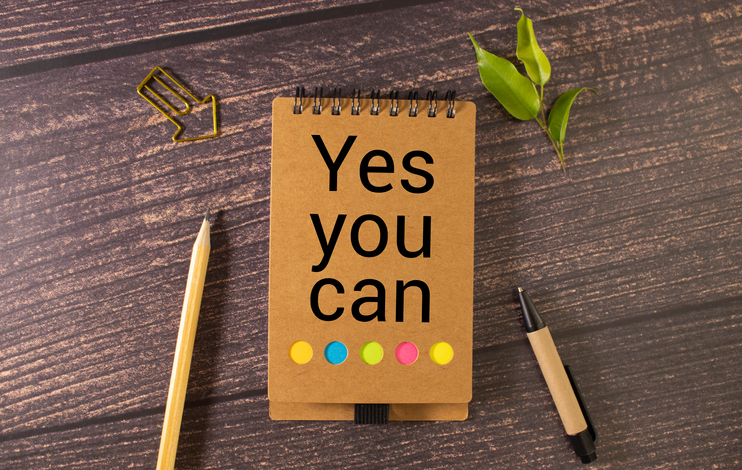 a wooden table and a notebook that says Yes you can